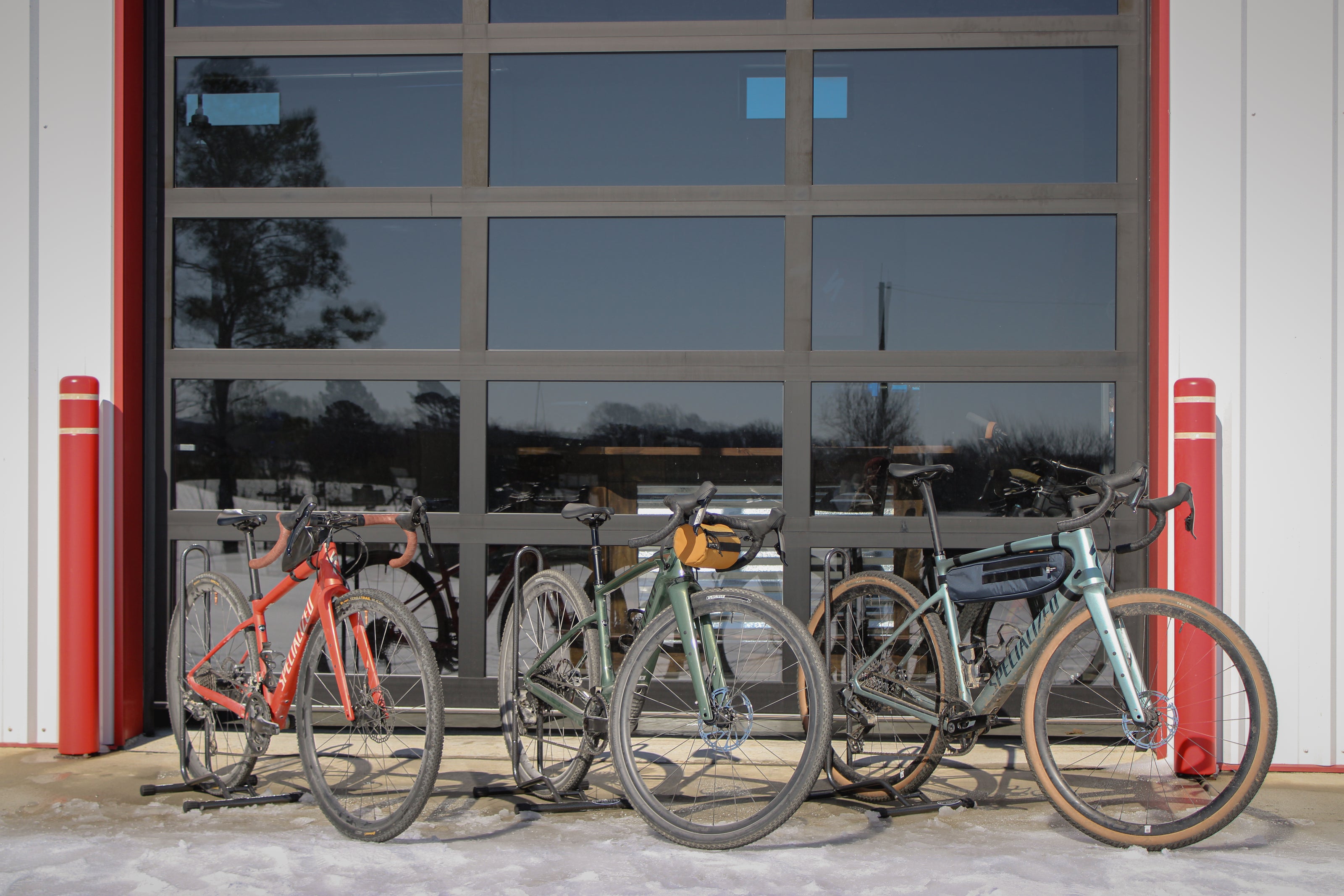 Bicycles parked in front of a large glass door with red frames.