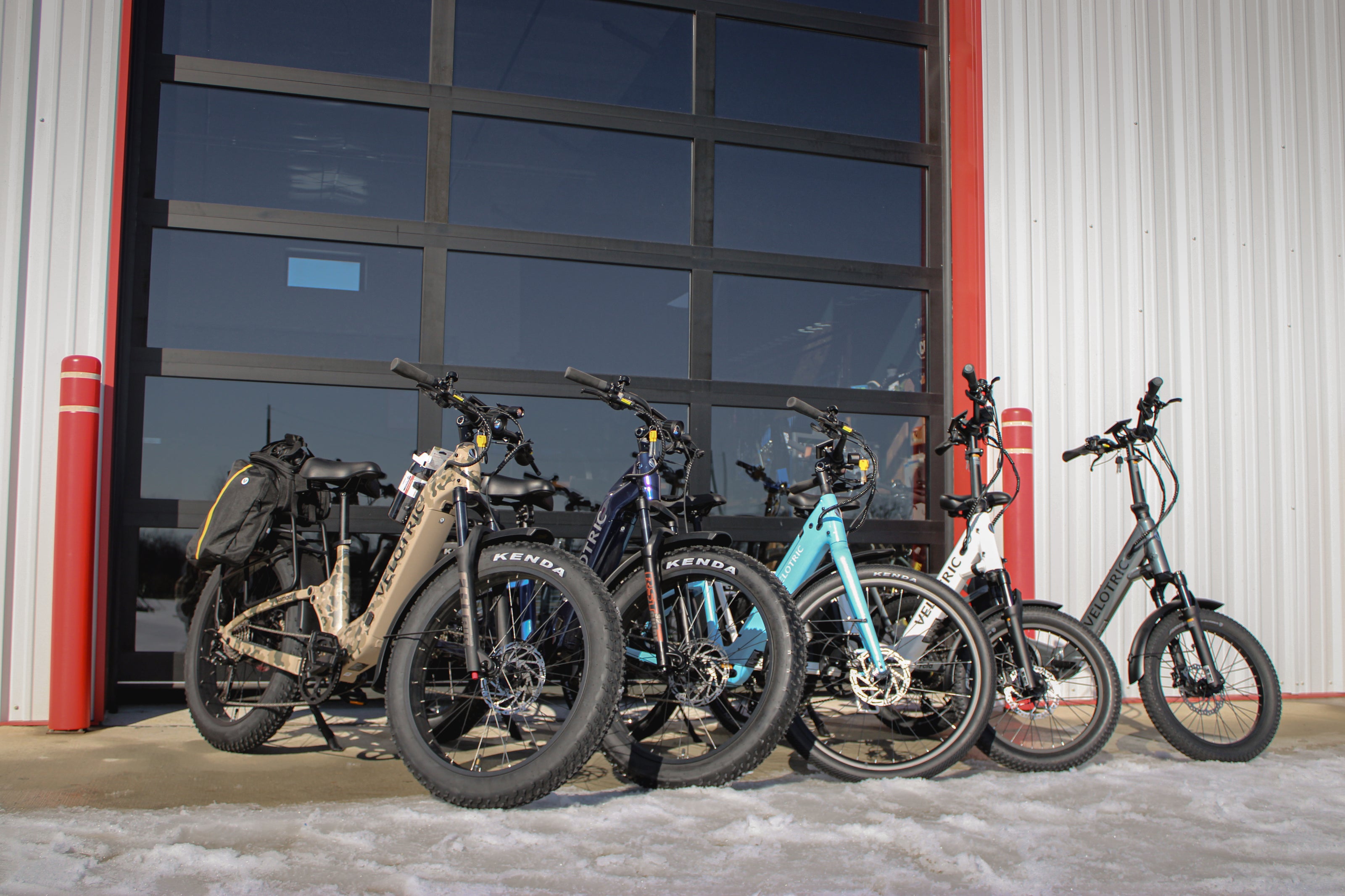 Multiple electric bicycles parked outside a building with large glass doors.